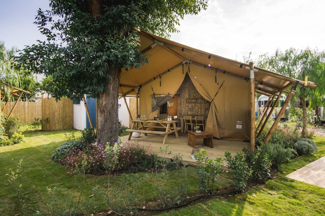 A glamping tent accommodation with wooden deck, furnished interior, and surrounding manicured gardens at the resort.
